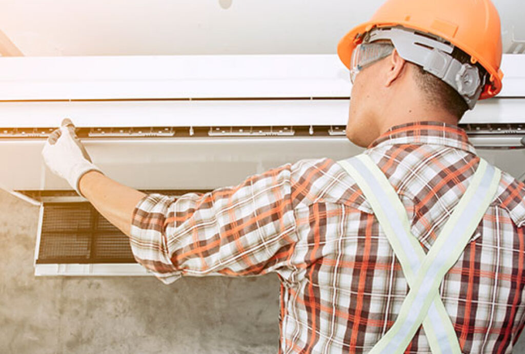 A man wearing protective head gear while servicing an air conditioner