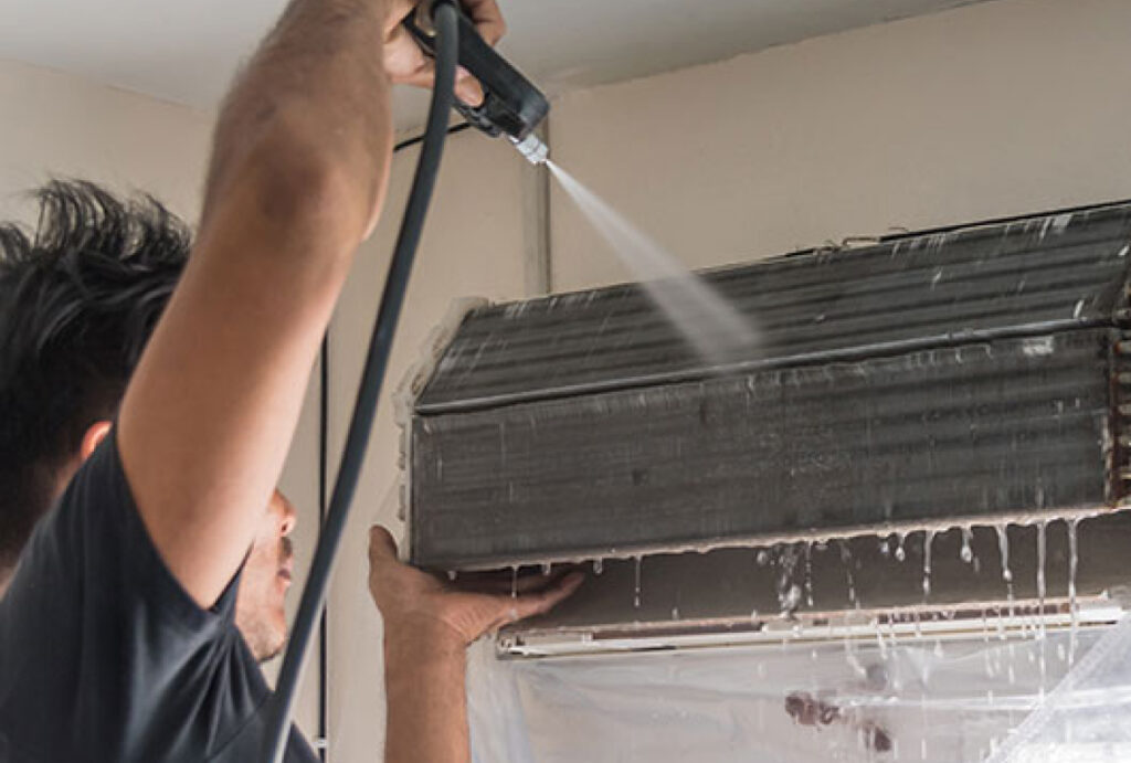A worker cleaning and disinfecting an air conditioner with a power hose