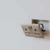 Damaged electrical socket with exposed wiring on a white wall.