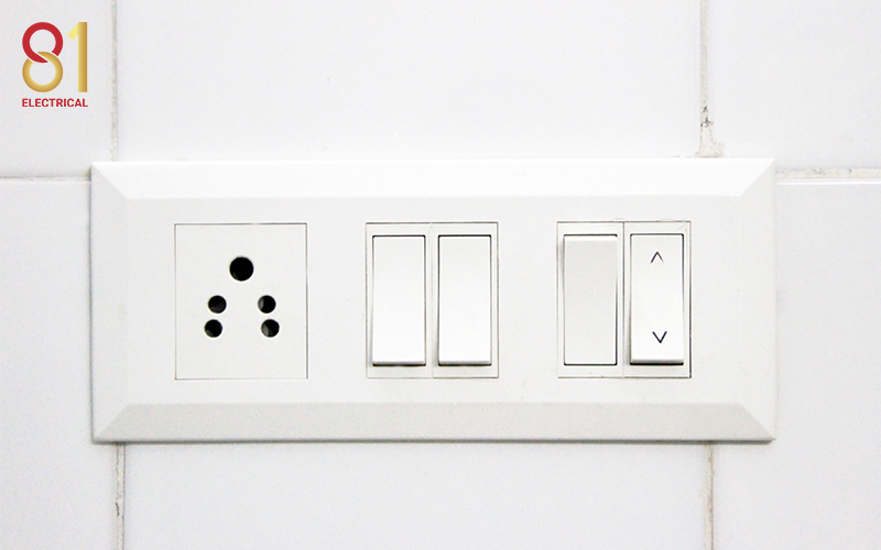 White electrical outlet with light switches on a tiled wall.