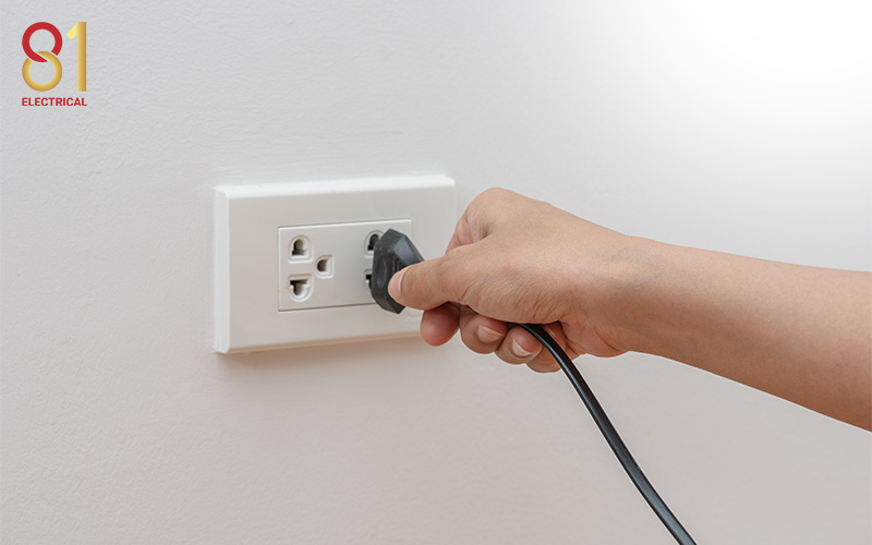 Hand unplugging a black cord from a wall outlet.