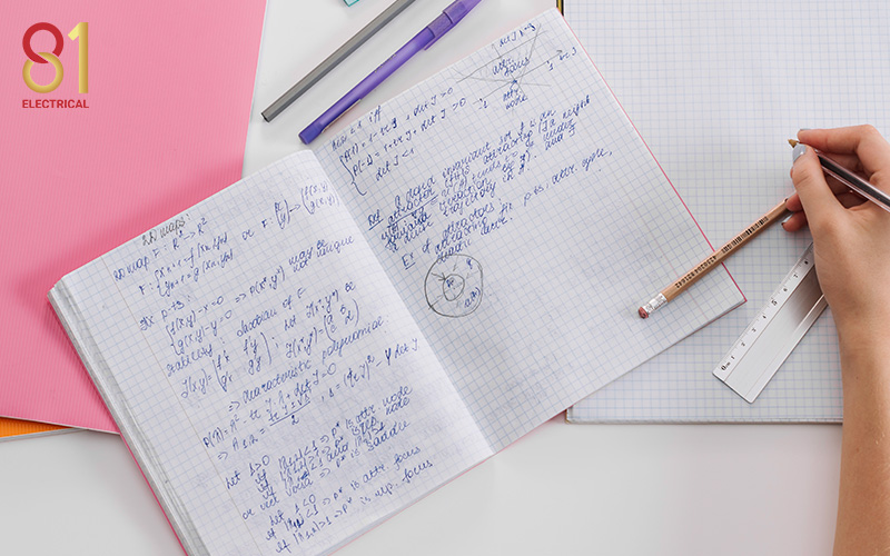Hand writing electrical notes and formulas in a notebook.