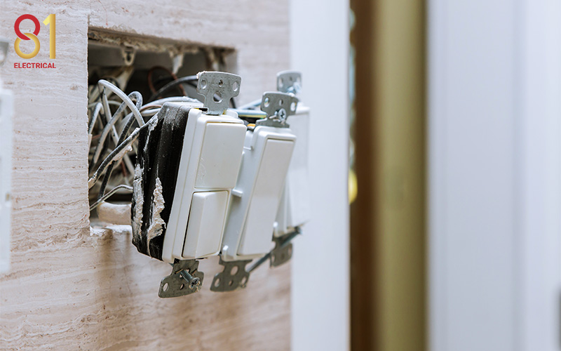 Damaged light switches with wires sticking out of the wall.