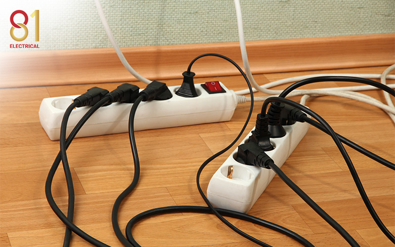 Multiple power strips overloaded with plugs on a wooden floor.